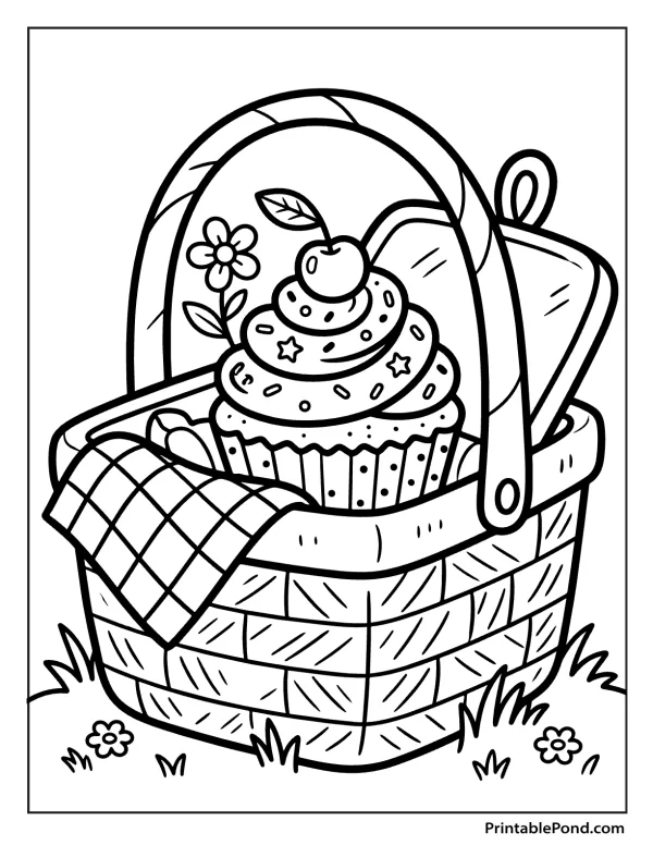 A cupcake with sprinkles and a cherry sits inside a woven picnic basket with a checkered cloth and a flower.