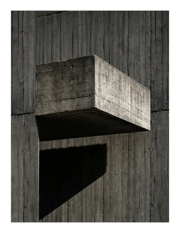 A concrete slab juts out from a textured concrete wall, casting a sharp shadow below.